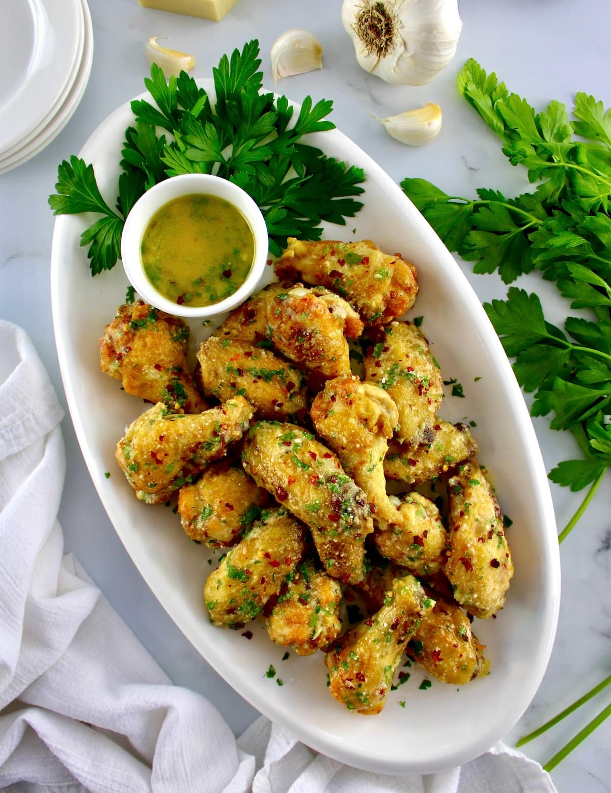 overhead view of Air Fryer Garlic Parmesan Wings on white platter with butter sauce on side and parsley
