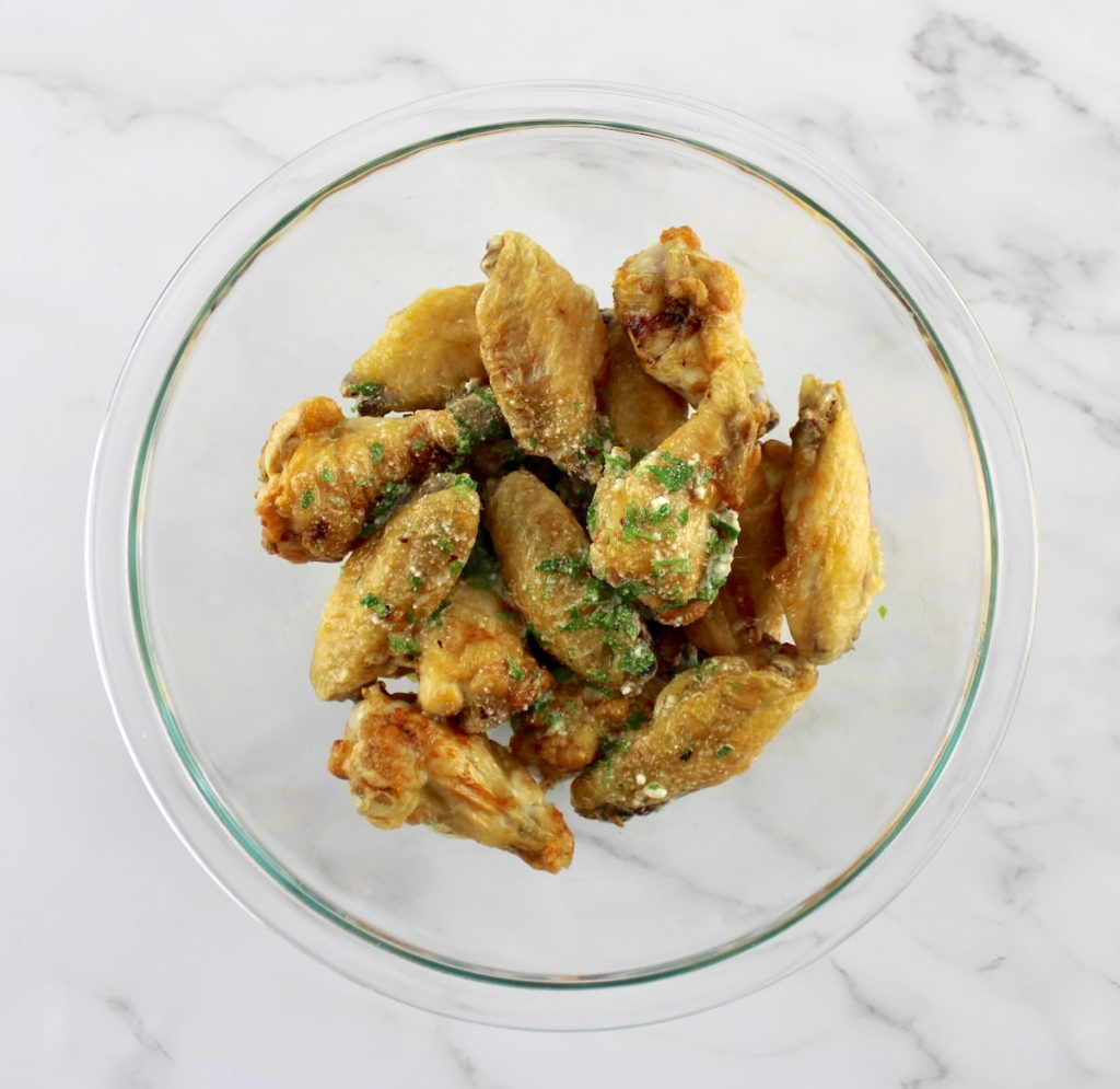 chicken wings in glass bowl with garlic parmesan sauce poured on top