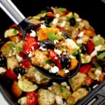 Air Fryer Greek Chicken Bites in black serving spoon held up over air fryer basket