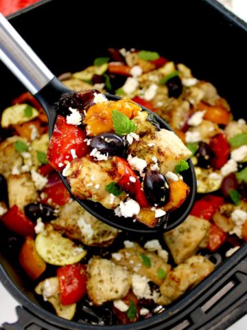 Air Fryer Greek Chicken Bites in black serving spoon held up over air fryer basket