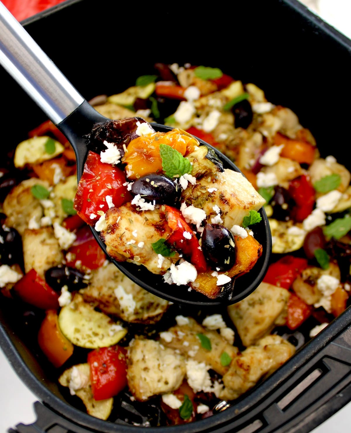 Air Fryer Greek Chicken Bites in black serving spoon held up over air fryer basket