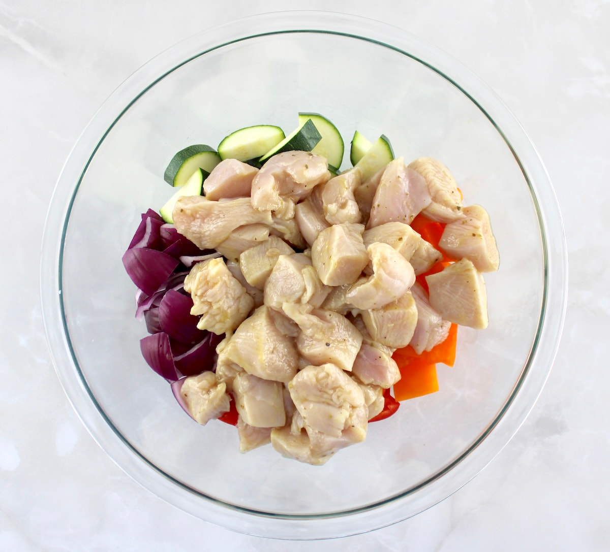 marinate chicken bites, chopped zucchini, red onion, red and orange bell peppers in glass bowl
