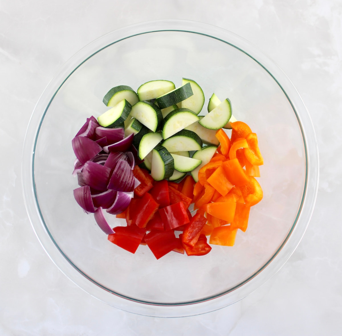 chopped zucchini, red onion, red and orange bell peppers in glass bowl