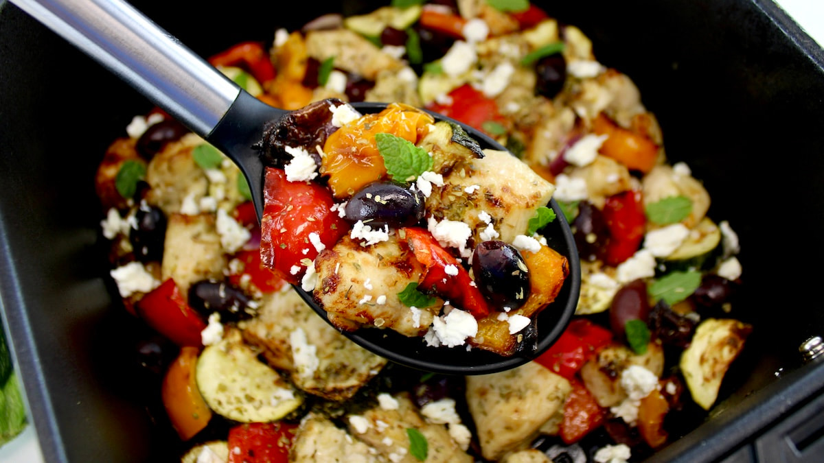 Air Fryer Greek Chicken Bites in black serving spoon held up over air fryer basket