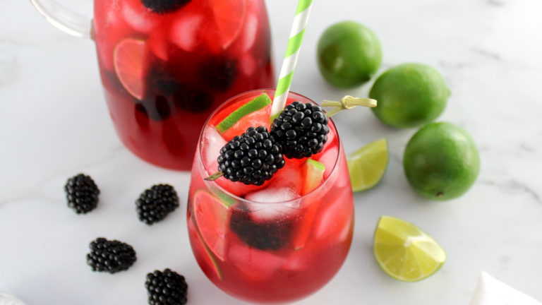 horizontal image of blackberry limeade in a glass with fresh blackberry garnish