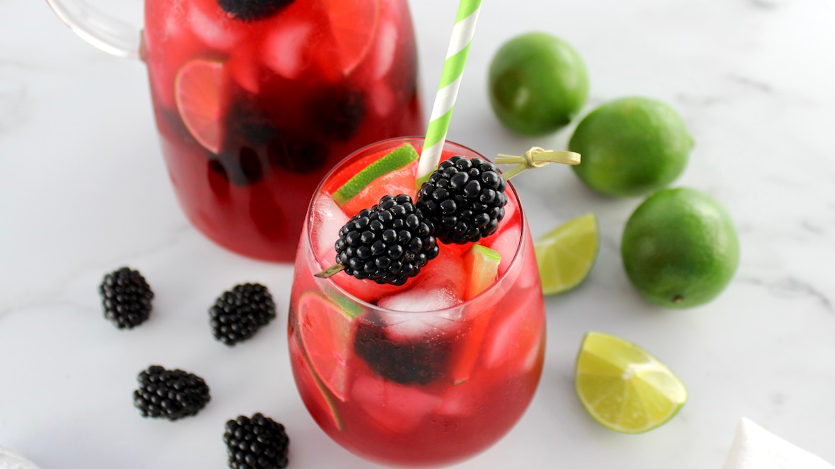 horizontal image of blackberry limeade in a glass with fresh blackberry garnish