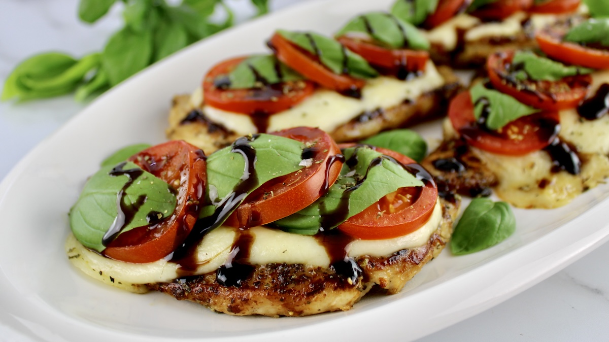 closeup of Chicken Caprese on white oval platter with balsamic glaze drizzled on top