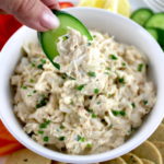 Cold Crab Dip in white bowl being scooped with cucumber