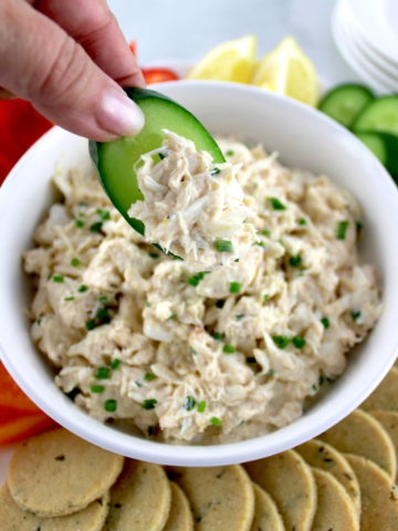 Cold Crab Dip in white bowl being scooped with cucumber