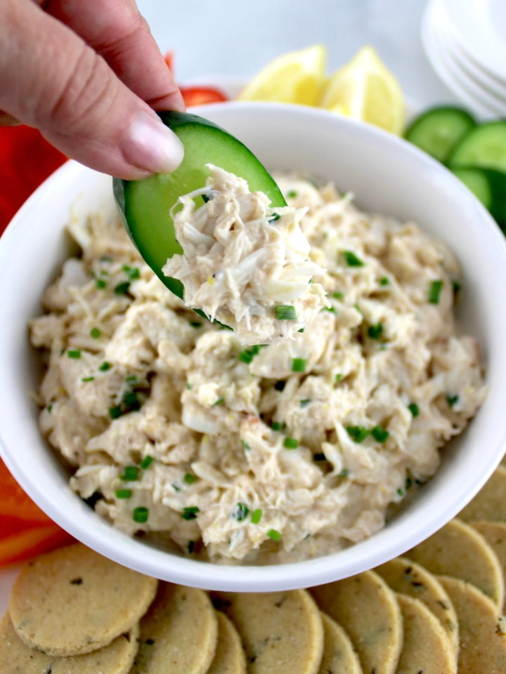 Cold Crab Dip in white bowl being scooped with cucumber