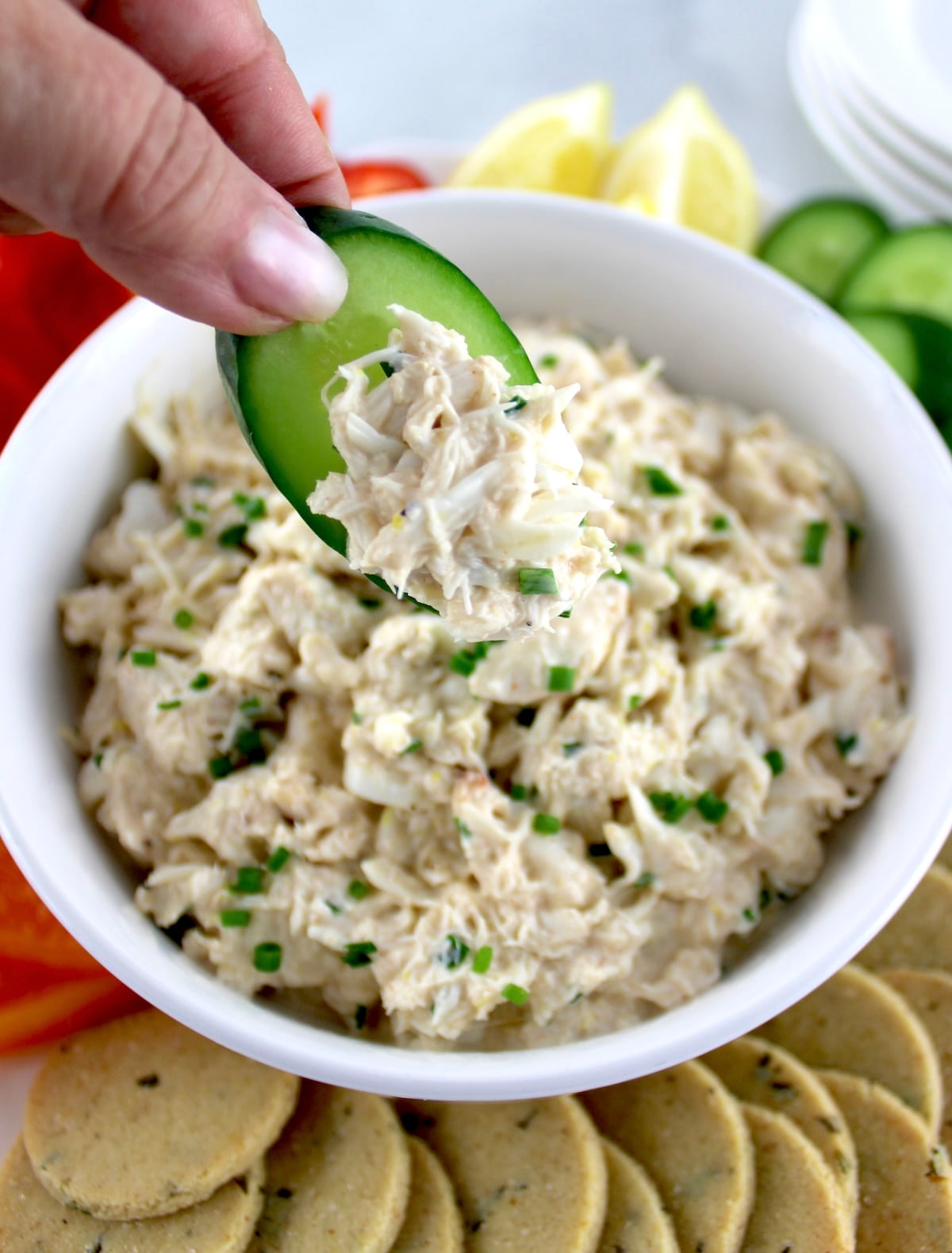 Cold Crab Dip in white bowl being scooped with cucumber