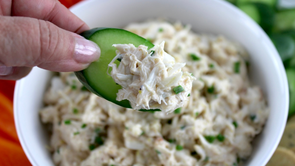 Cold Crab Dip in white bowl being scooped with cucumber