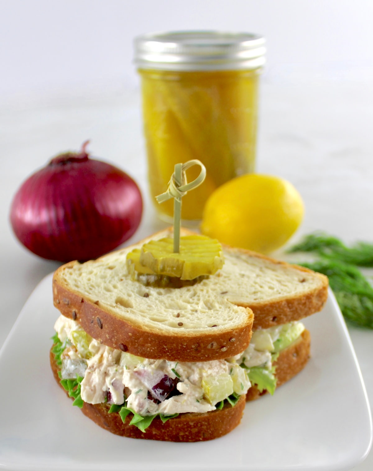 Dill Pickle Chicken Salad sandwich with pickles, red onion and lemon in back