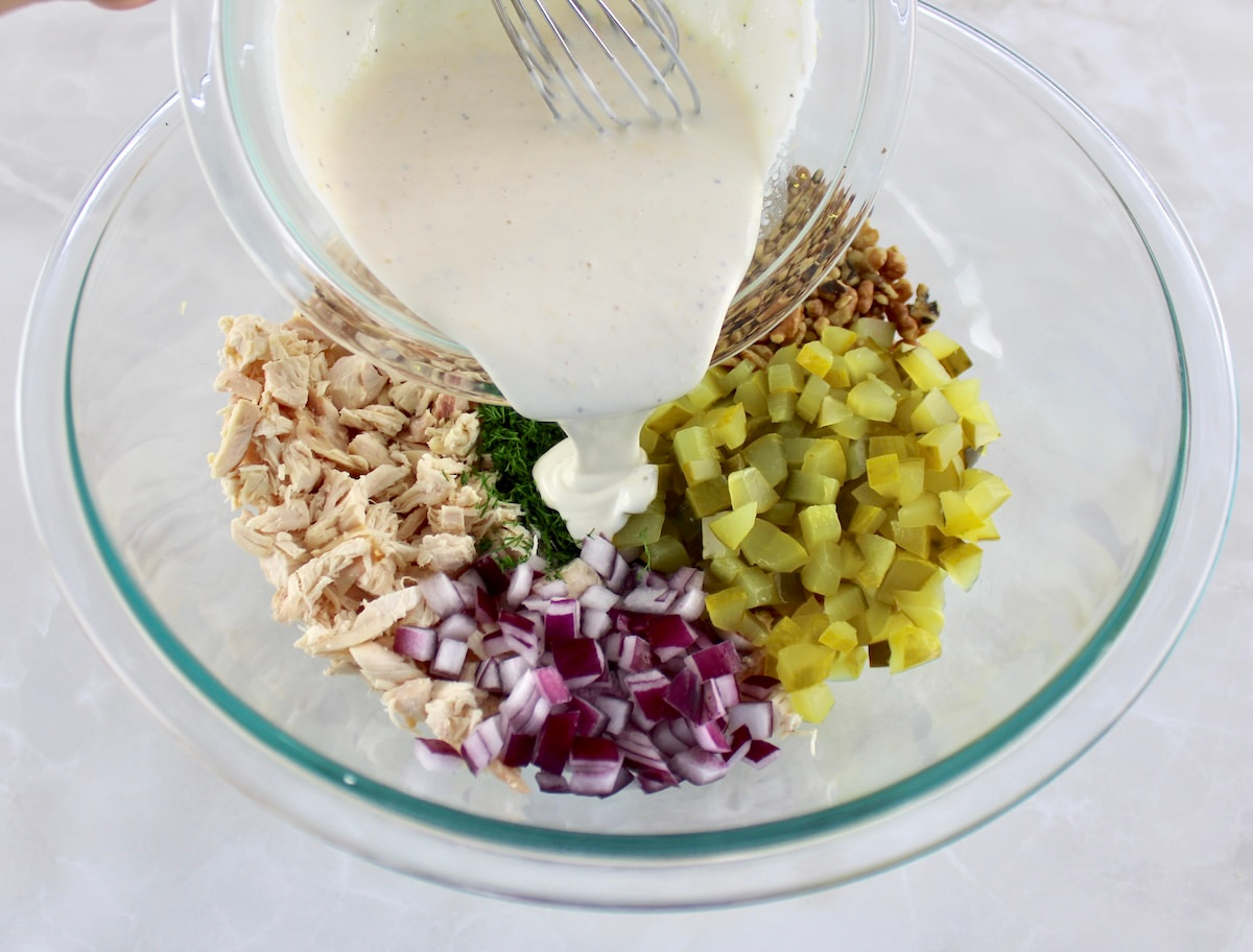 Dill Pickle Chicken Salad ingredients in glass bowl unmixed in sections with dressing being poured over top