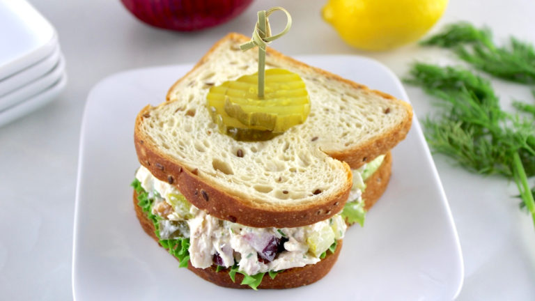 Dill Pickle Chicken Salad sandwich on white plate with toothpick and pickles on top