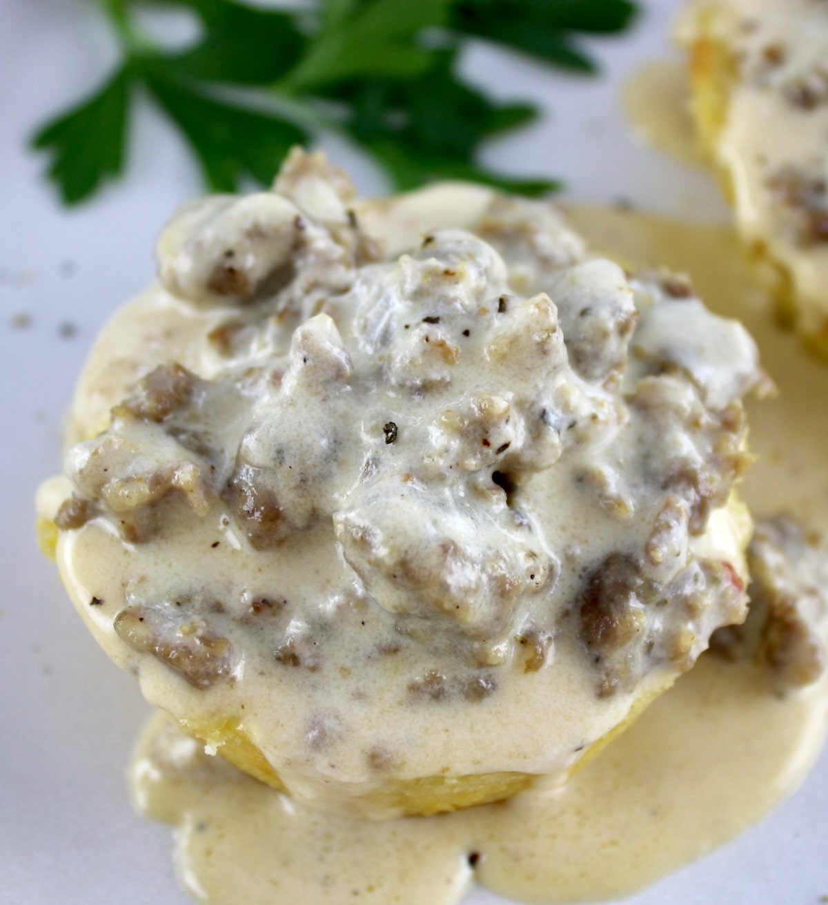 closeup of Keto Biscuits and Gravy on white plate with parsley in back