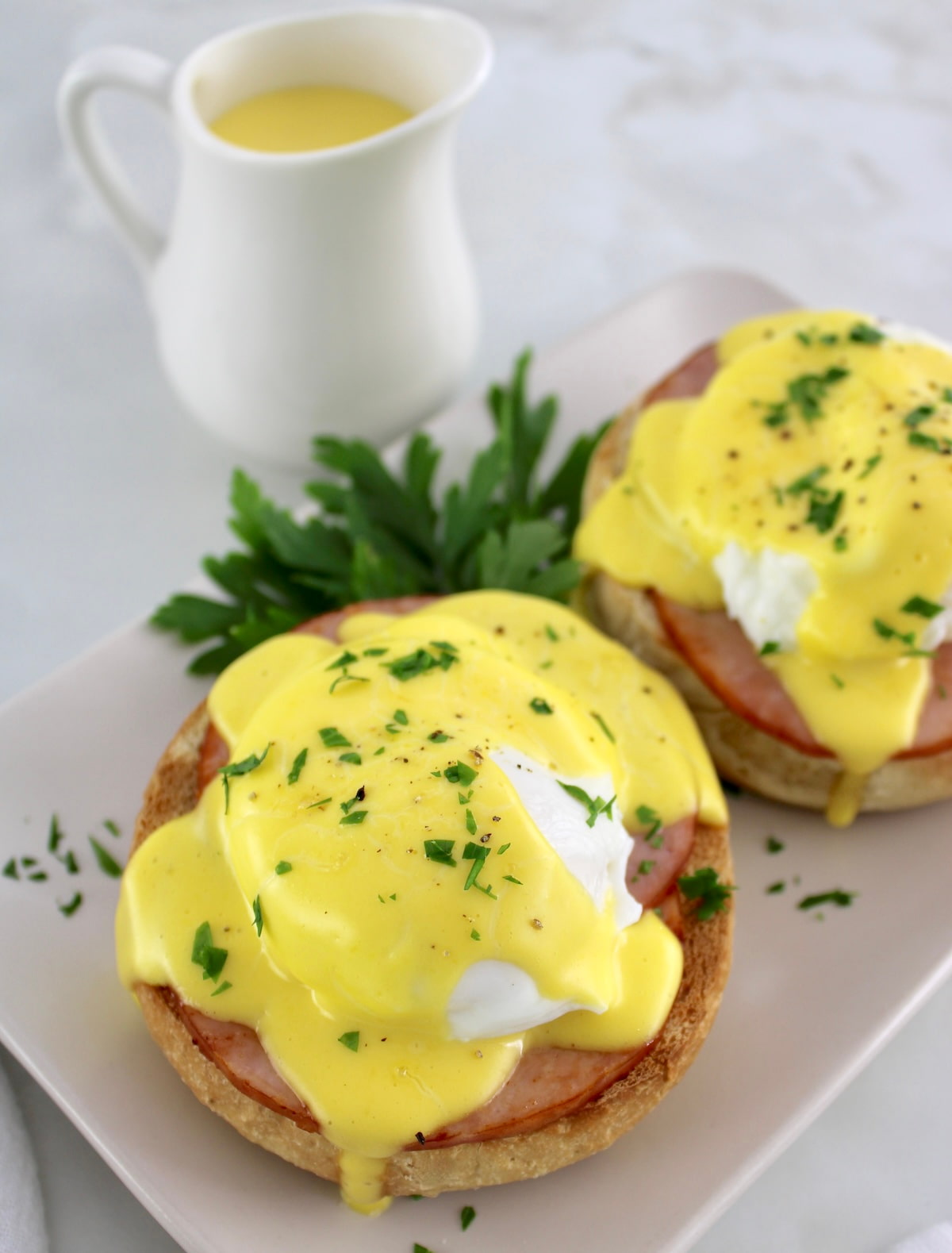 closeup of Keto Eggs Benedict on plate with hollandaise dripping off the side and more sauce in back