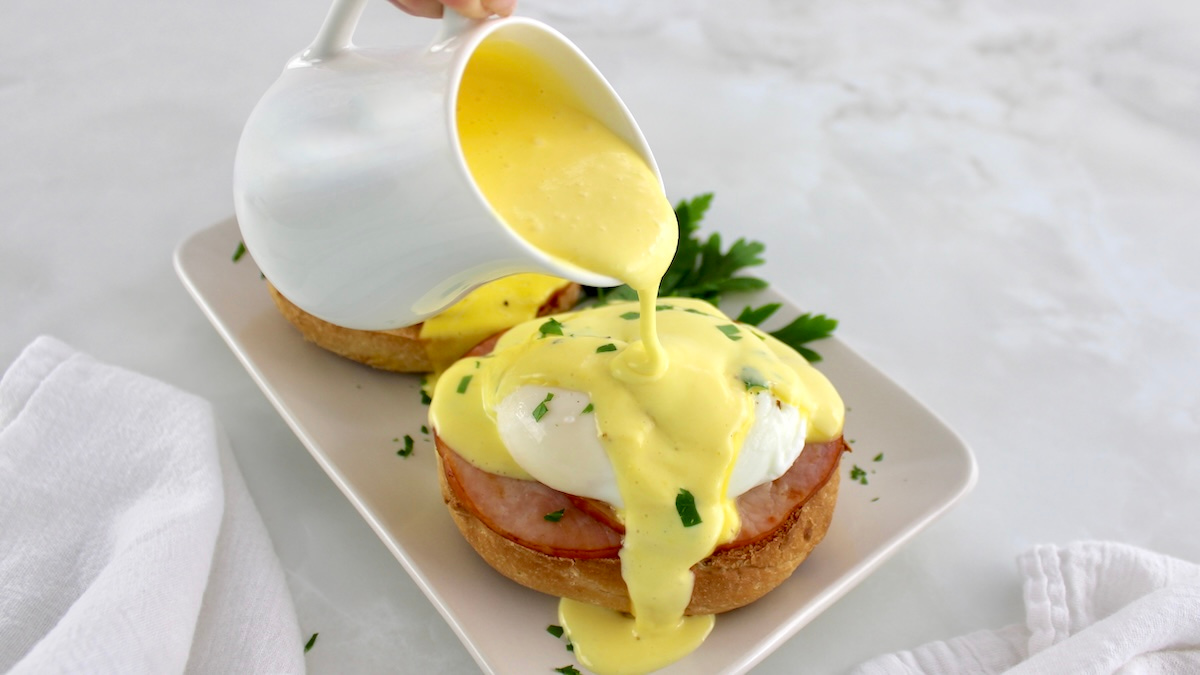 hollandaise sauce being poured over Keto Eggs Benedict