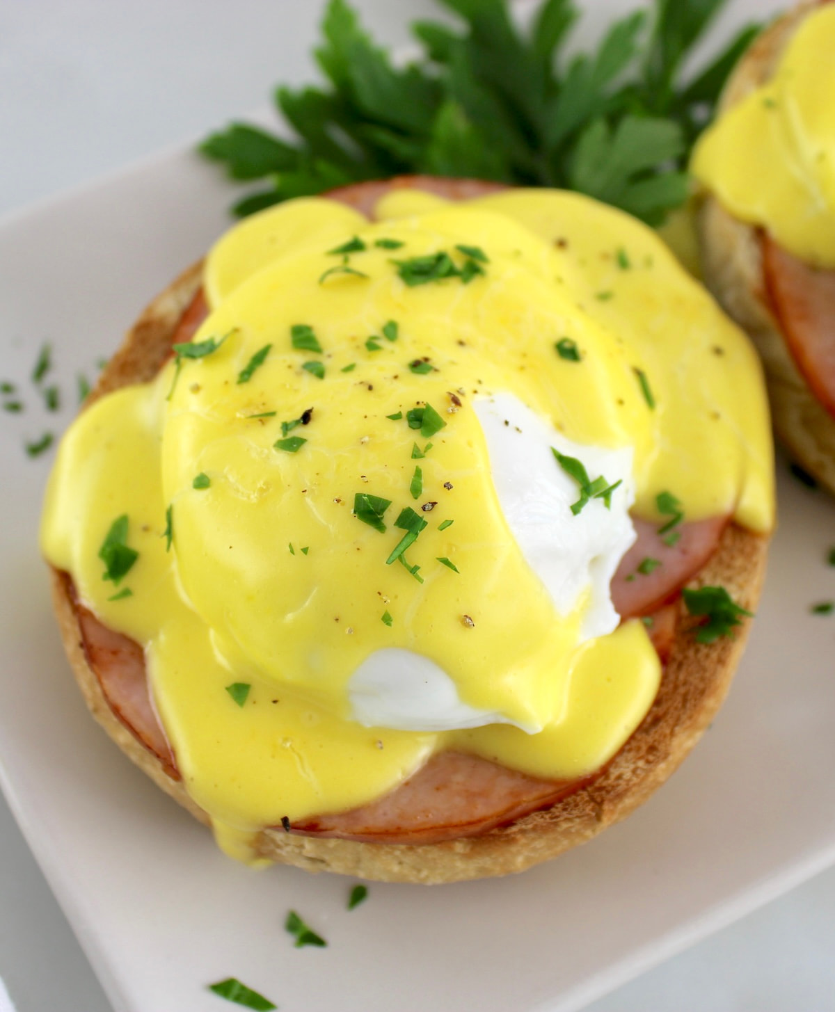 closeup of Keto Eggs Benedict on plate with hollandaise dripping off the side and more sauce in back