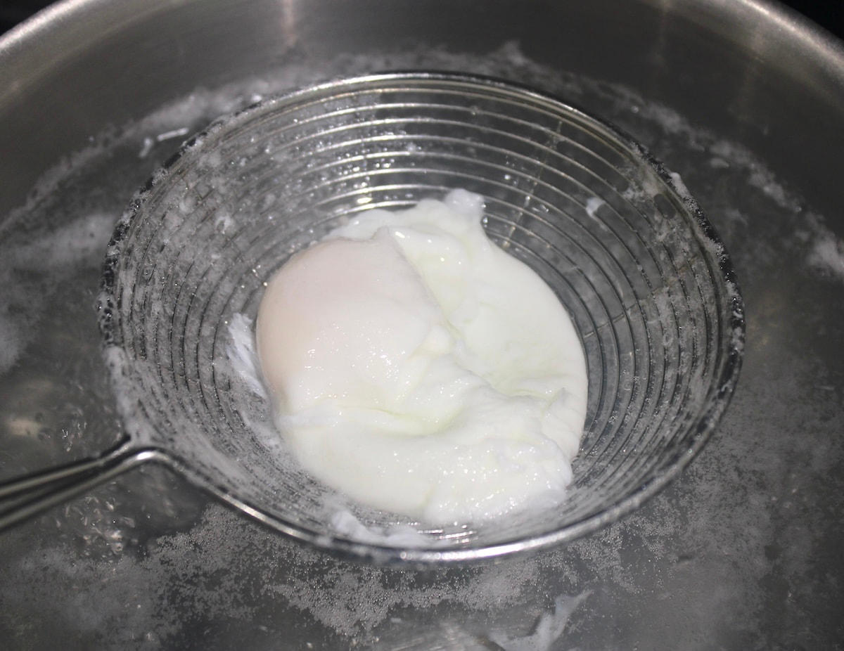 poached egg in spider over saucepan of boiling water