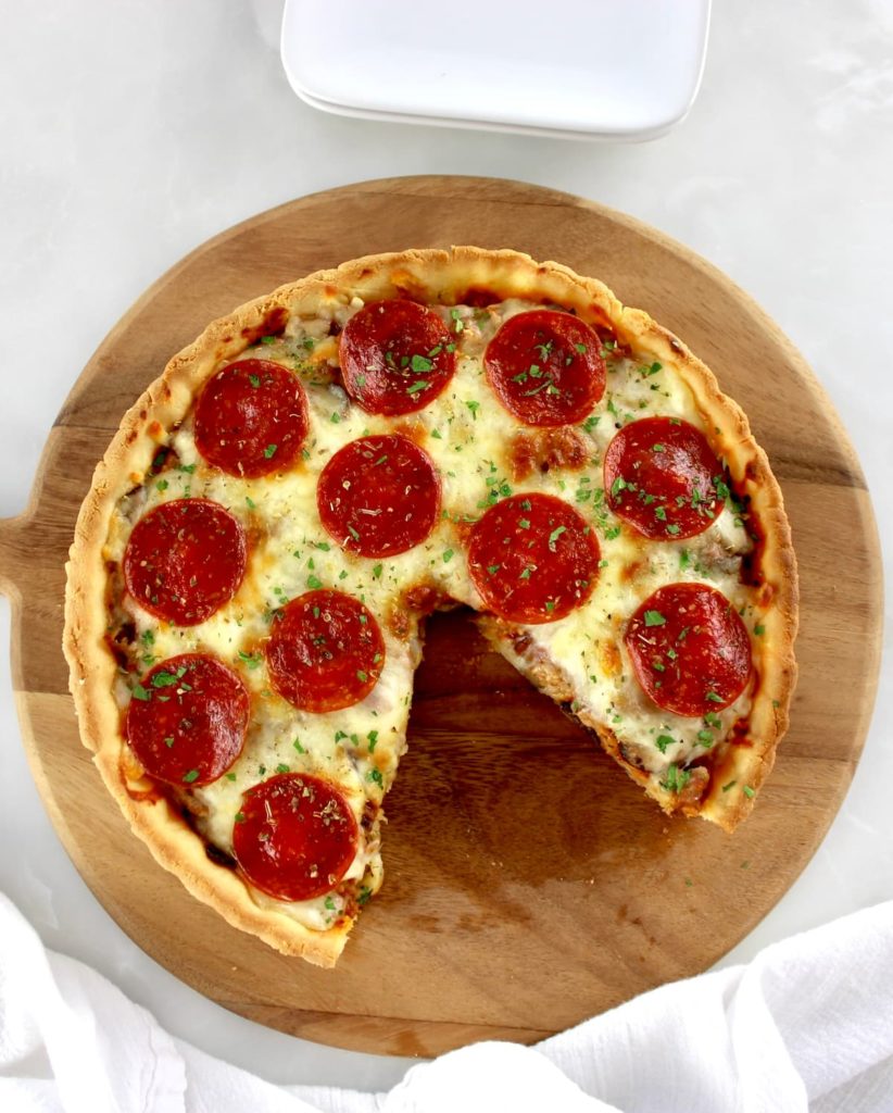overhead view of Keto Sausage and Pepperoni Pizza Pie on wooden peel with slice missing