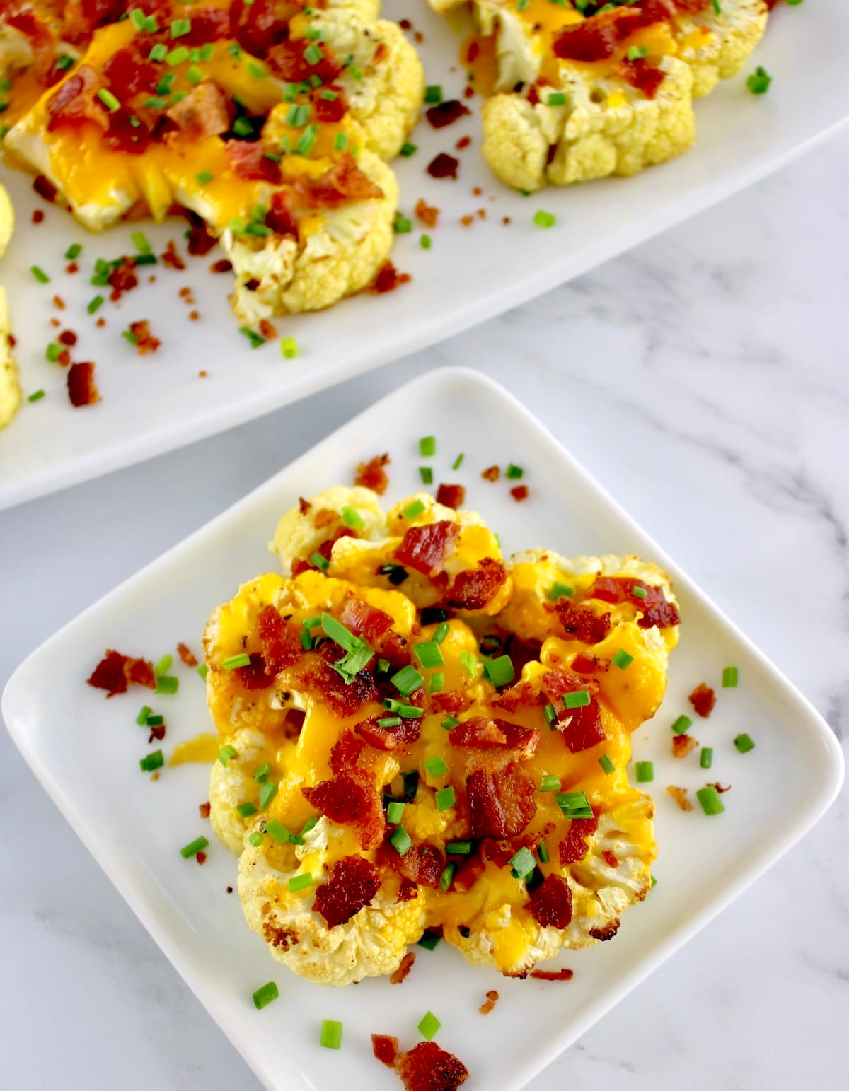 Loaded Cauliflower Steak on white plate with crumbled bacon and chives