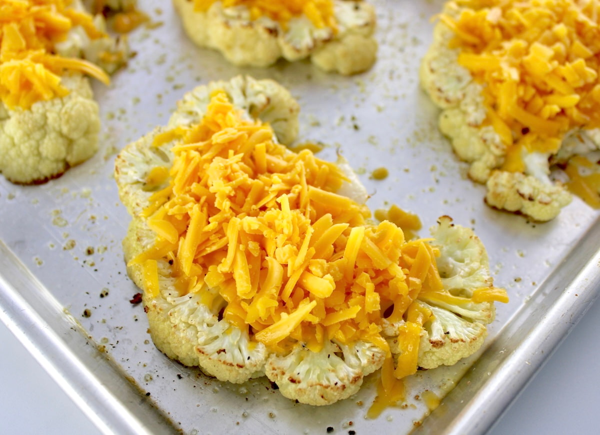 roasted cauliflower steaks on baking sheet with shredded cheddar cheese on top