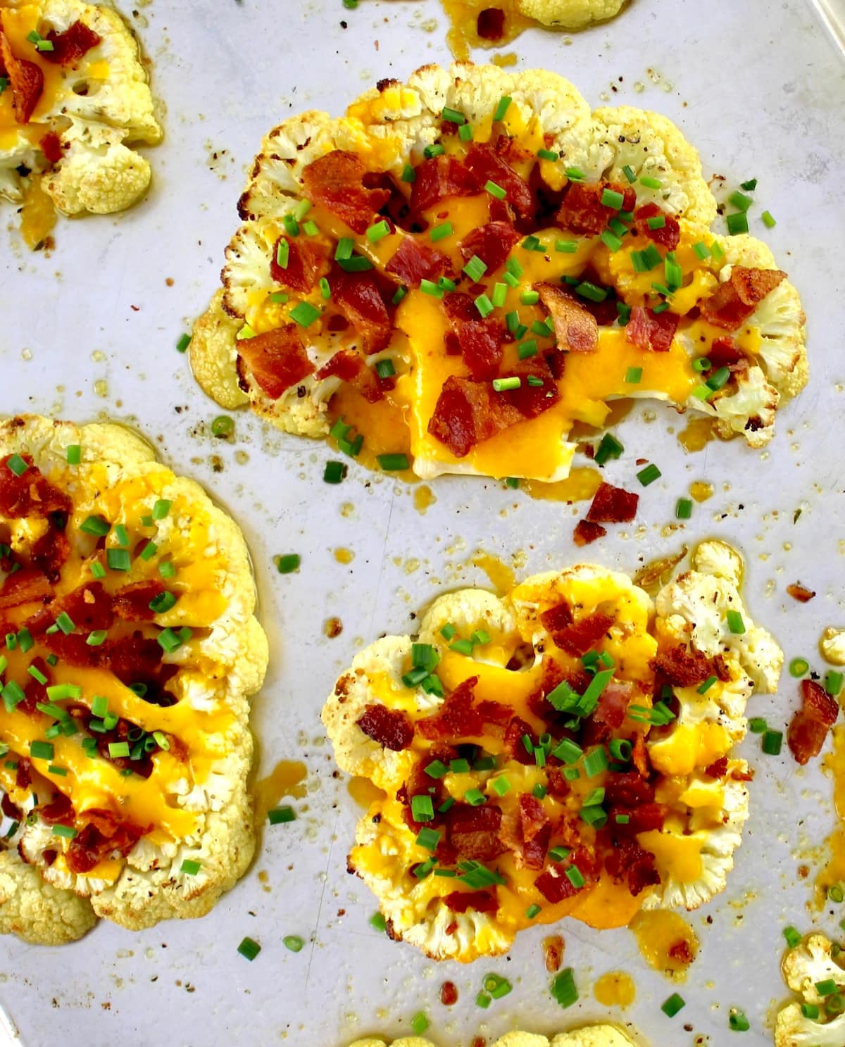 Loaded Cauliflower Steaks on baking sheet with crumbled bacon and chives on top