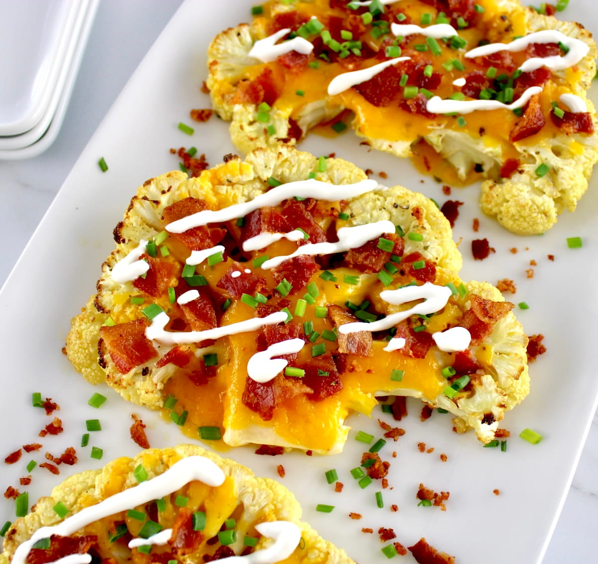 closeup of Loaded Cauliflower Steaks on white plate with sour cream drizzle on top