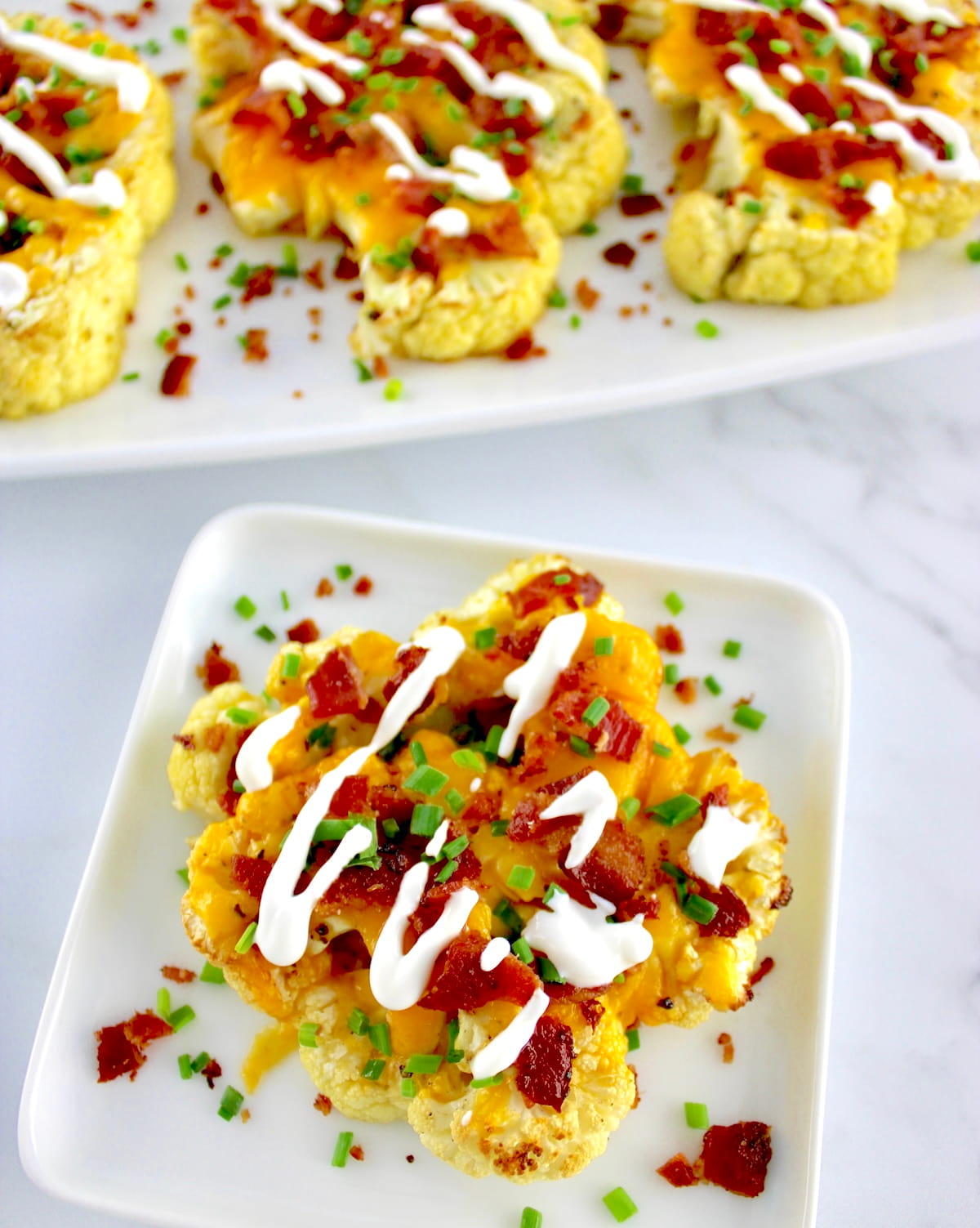 Loaded Cauliflower Steak on white plate with sour cream drizzle on top