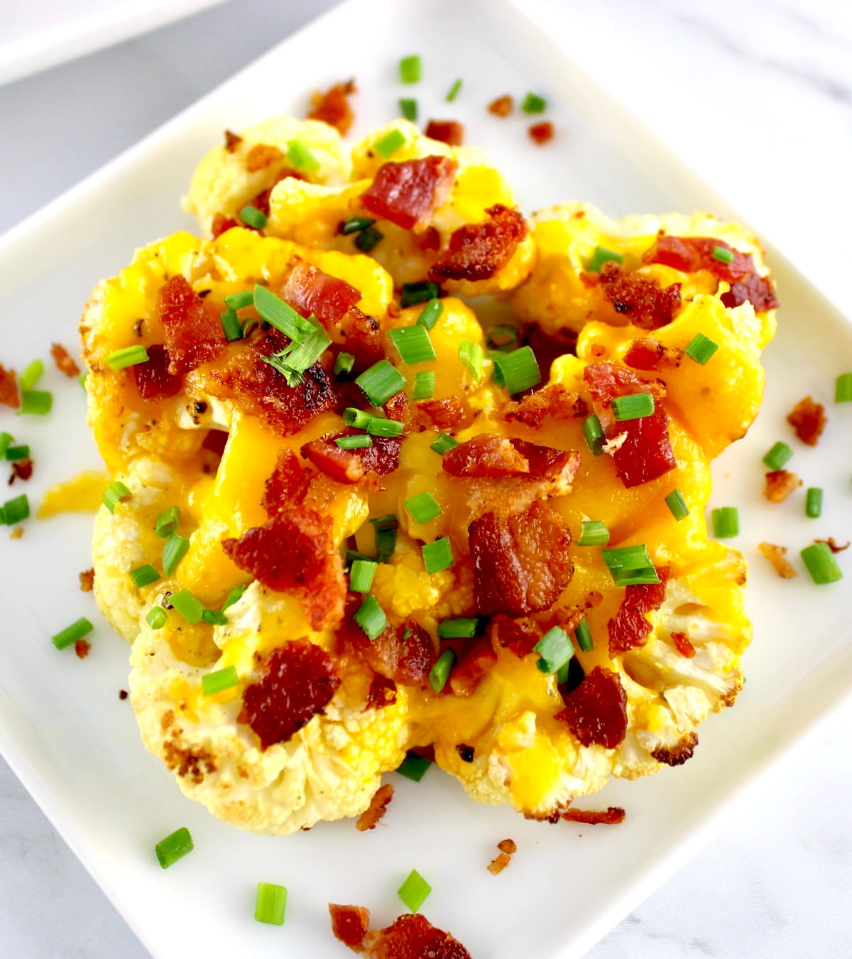 closeup of Loaded Cauliflower Steak on white plate with crumbled bacon and chives on top