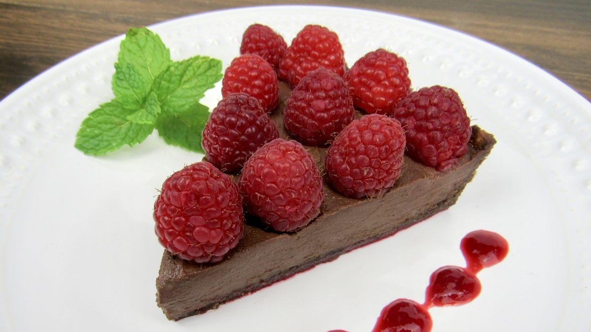 slice of No-Bake Chocolate Raspberry Tart on white plate with raspberries on top and mint sprig on side