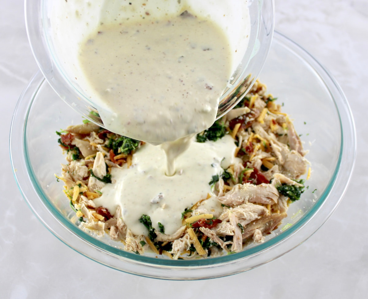 bacon ranch dressing being poured over chicken, cheddar cheese and bacon in glass bowl