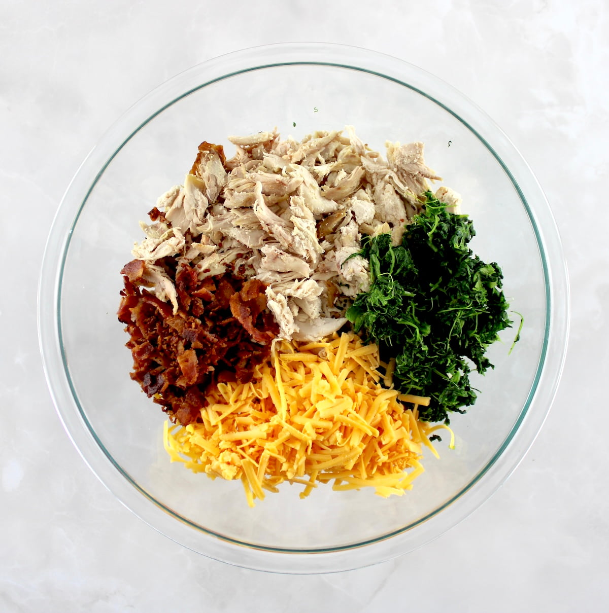 chopped cooked chicken, bacon, shredded cheddar and spinach in glass bowl in sections