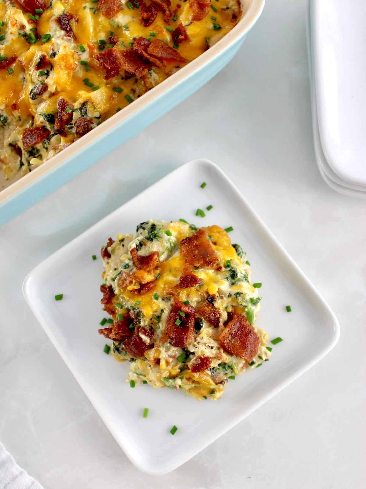 overhead view of Bacon Ranch Chicken Casserole on white square plate with casserole in back