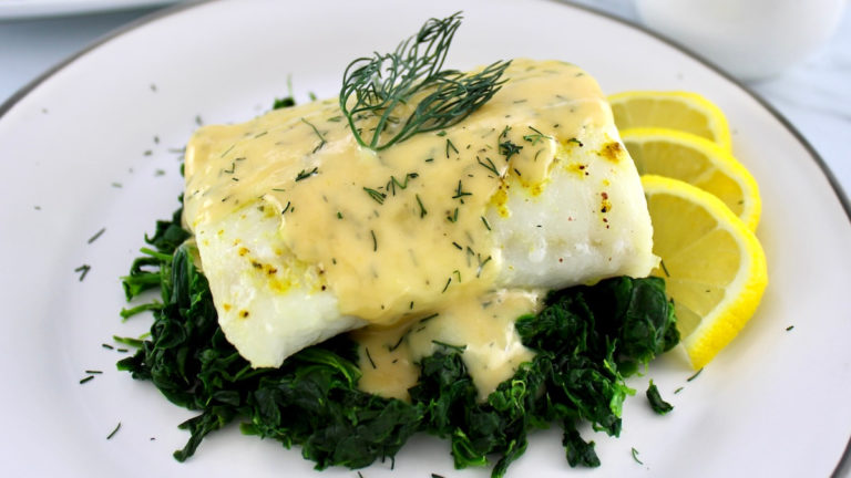 Baked Cod with Lemon Beurre Blanc over spinach on white plate