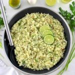 Chimichurri Cauliflower Rice in skillet with 3 lime slices and serving spoon on side