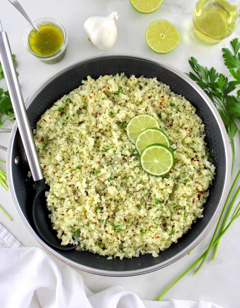 Chimichurri Cauliflower Rice in skillet with 3 lime slices and serving spoon on side