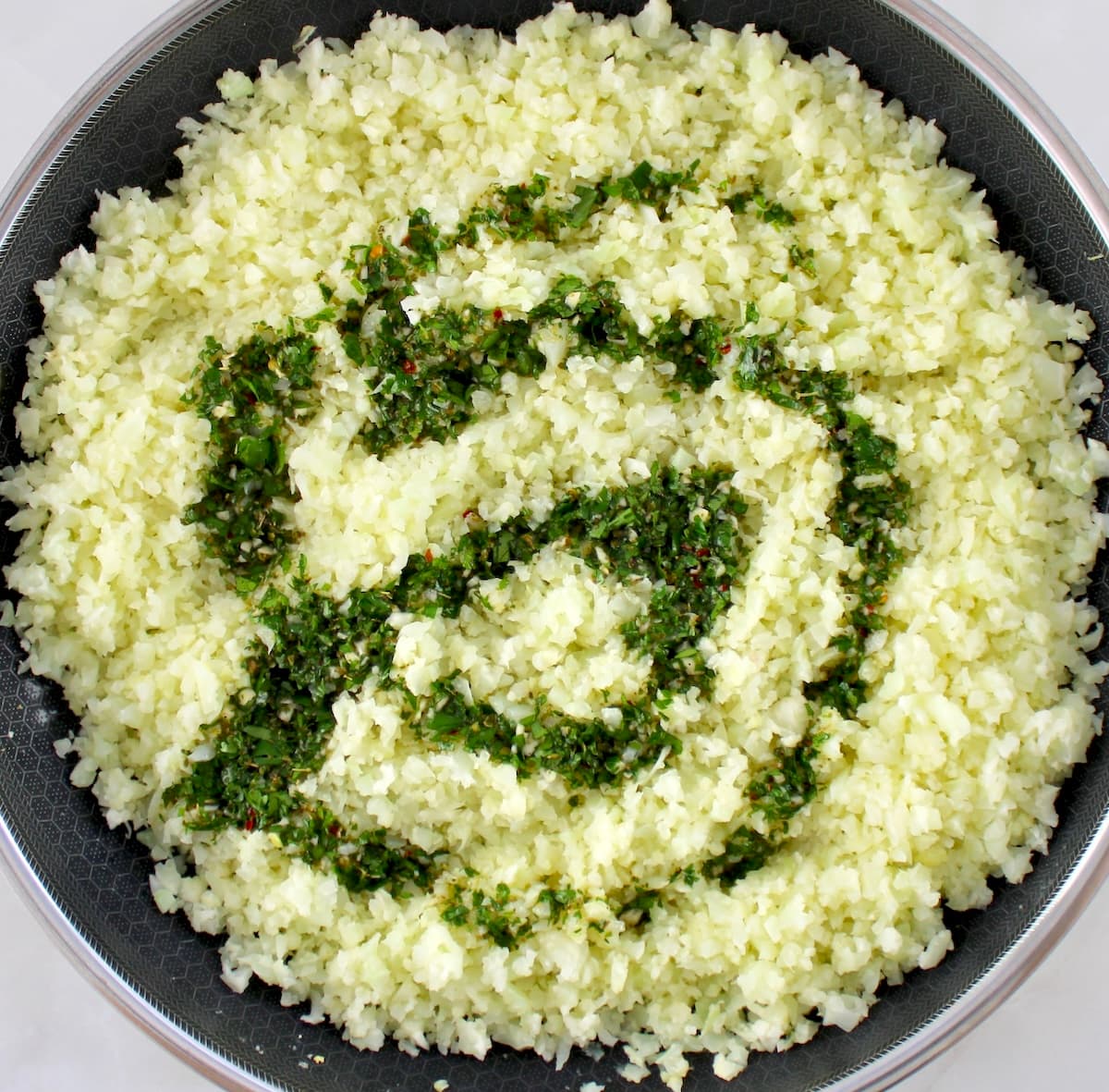 cauliflower rice cooking in skillet with drizzle of chimichurri sauce on top