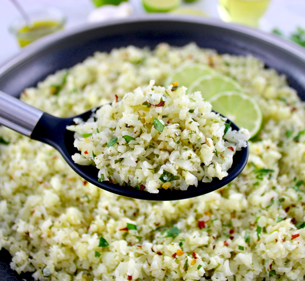 Chimichurri Cauliflower Rice in black serving spoon held up over skillet