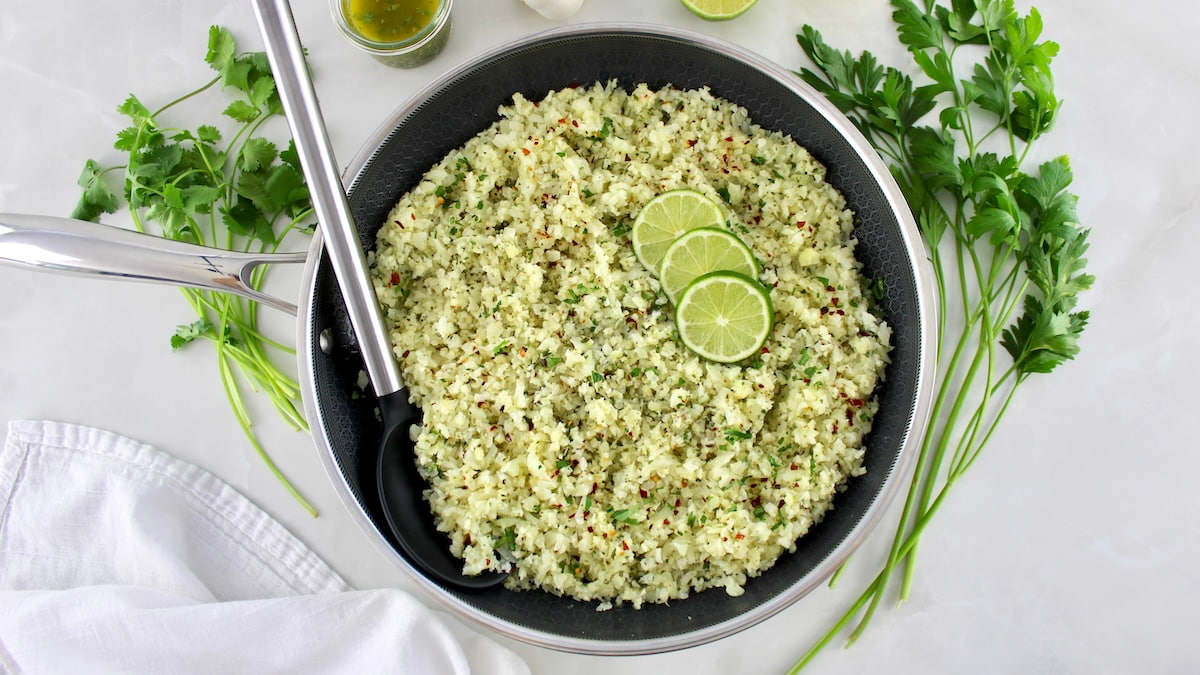 overhead view of Chimichurri Cauliflower Rice with 3 lime slices and black serving spoon on side