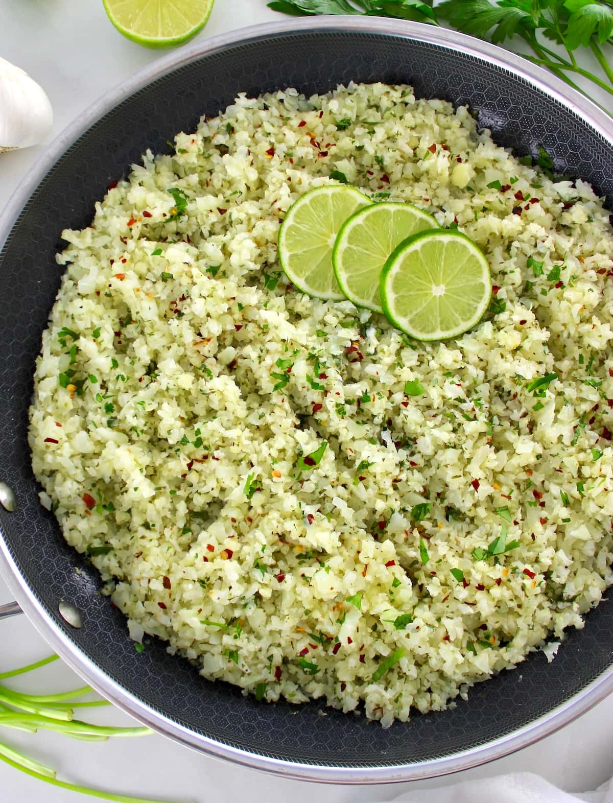 overhead view of Chimichurri Cauliflower Rice in skillet with lime slices