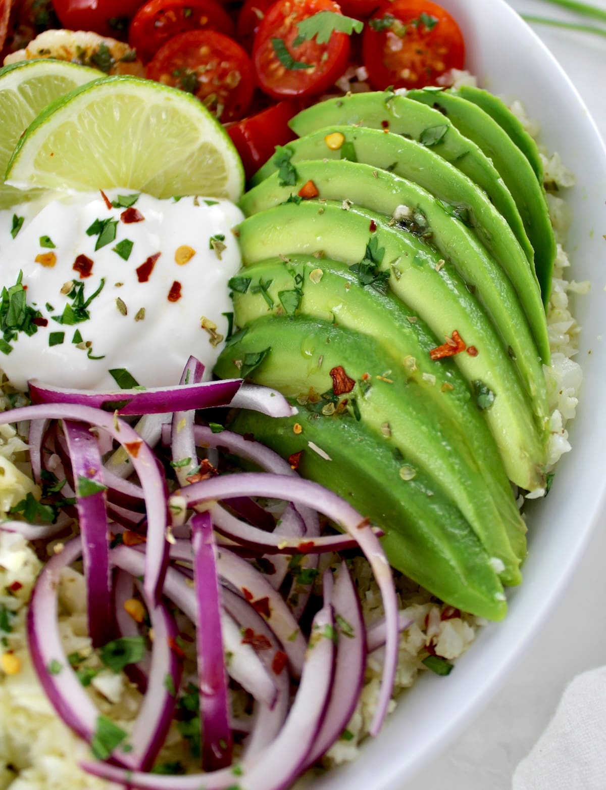 closeup of sliced red onion, avocado and sour cream in white bowl