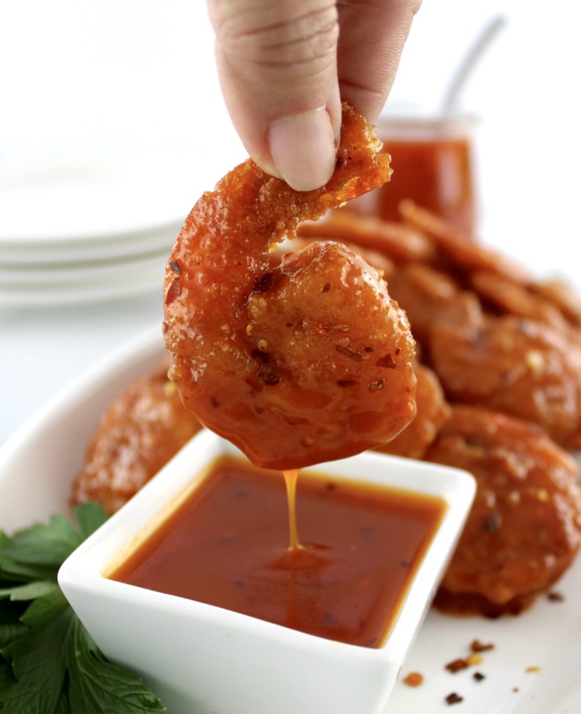 Hot Honey Fried Shrimp being dipped into hot honey sauce in white cup