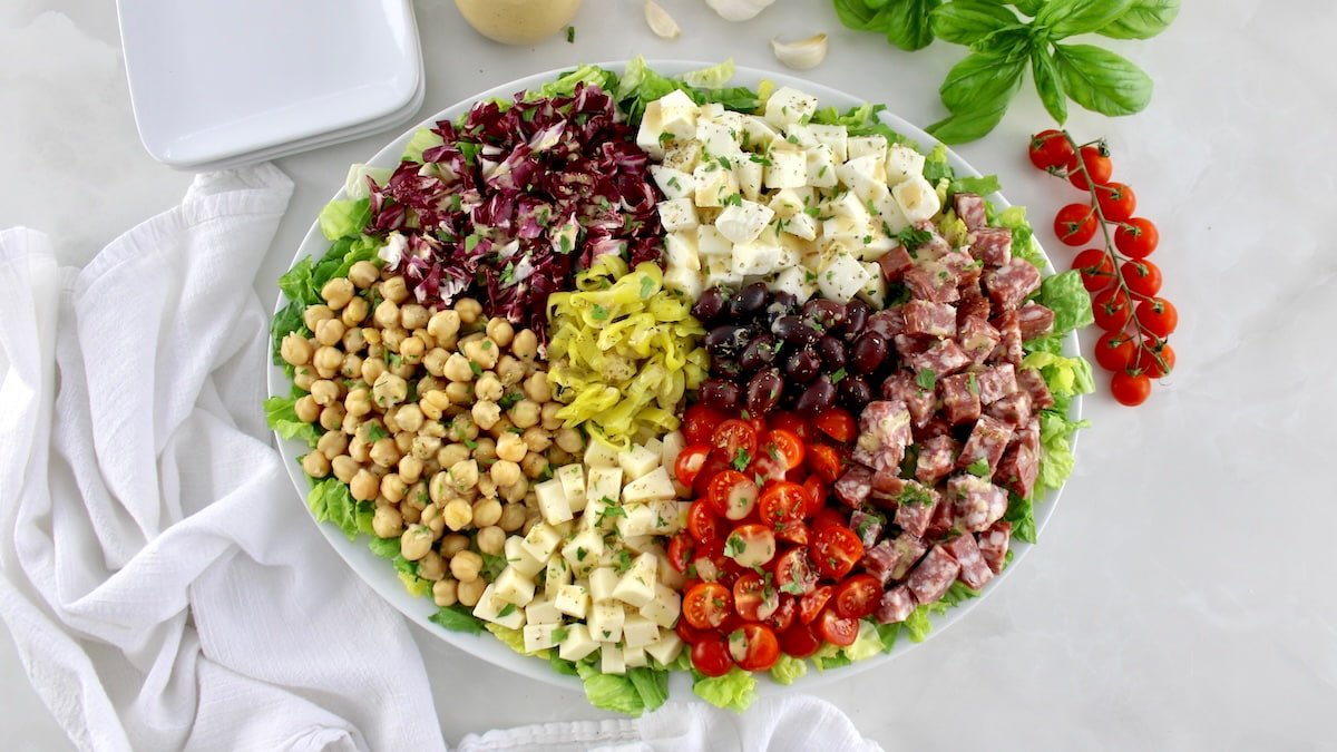 overhead view of Italian Chopped Salad on oval platter with dressing, basil and tomatoes in back
