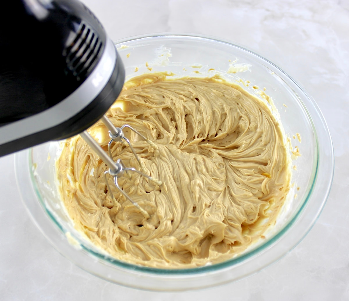 Keto Peanut Butter Frosting being whipped using hand mixer in glass bowl