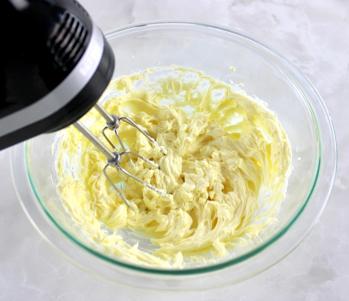 butter and mascarpone being whipped in glass bowl with hand mixer
