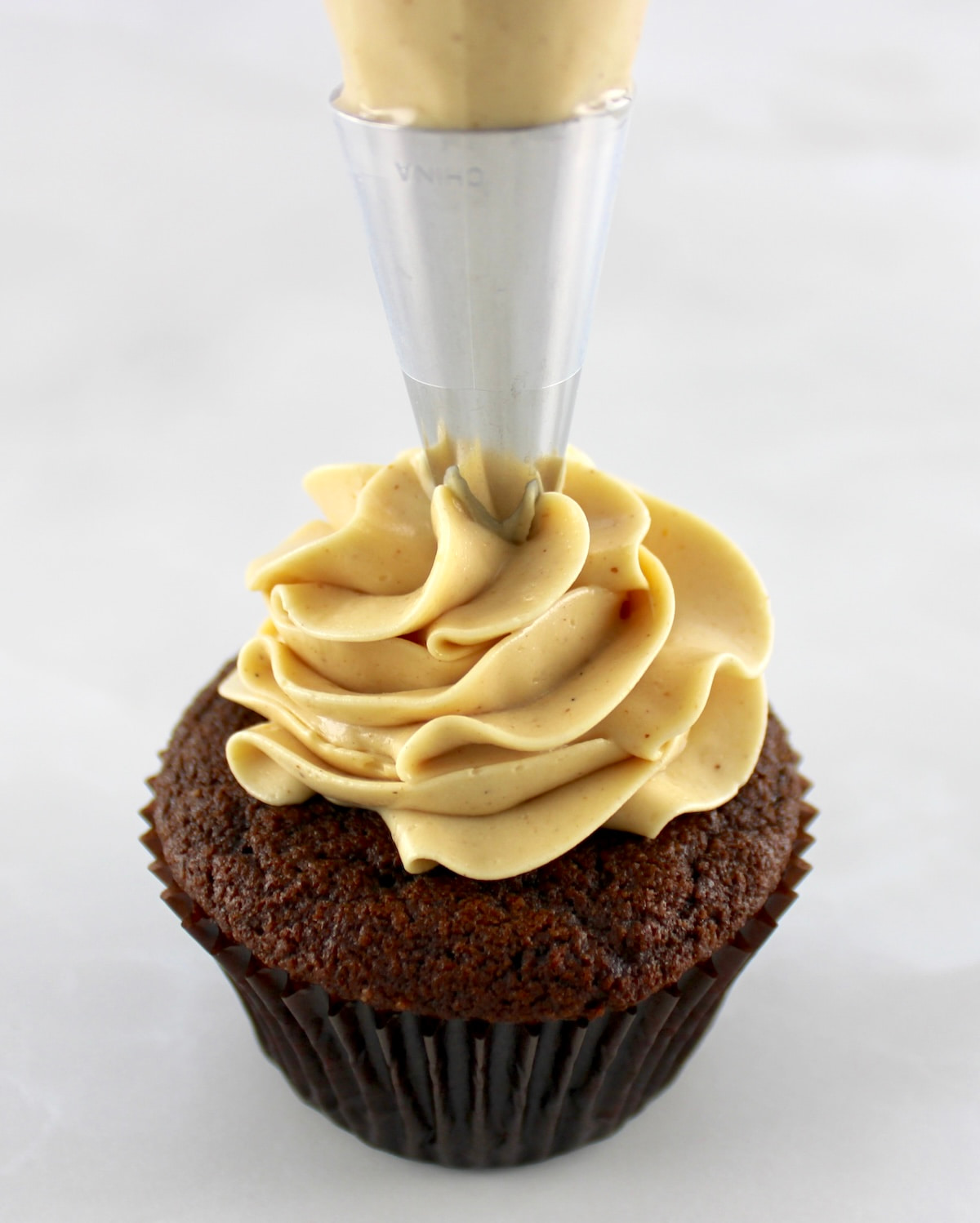 Keto Peanut Butter Frosting being piped onto chocolate cupcake