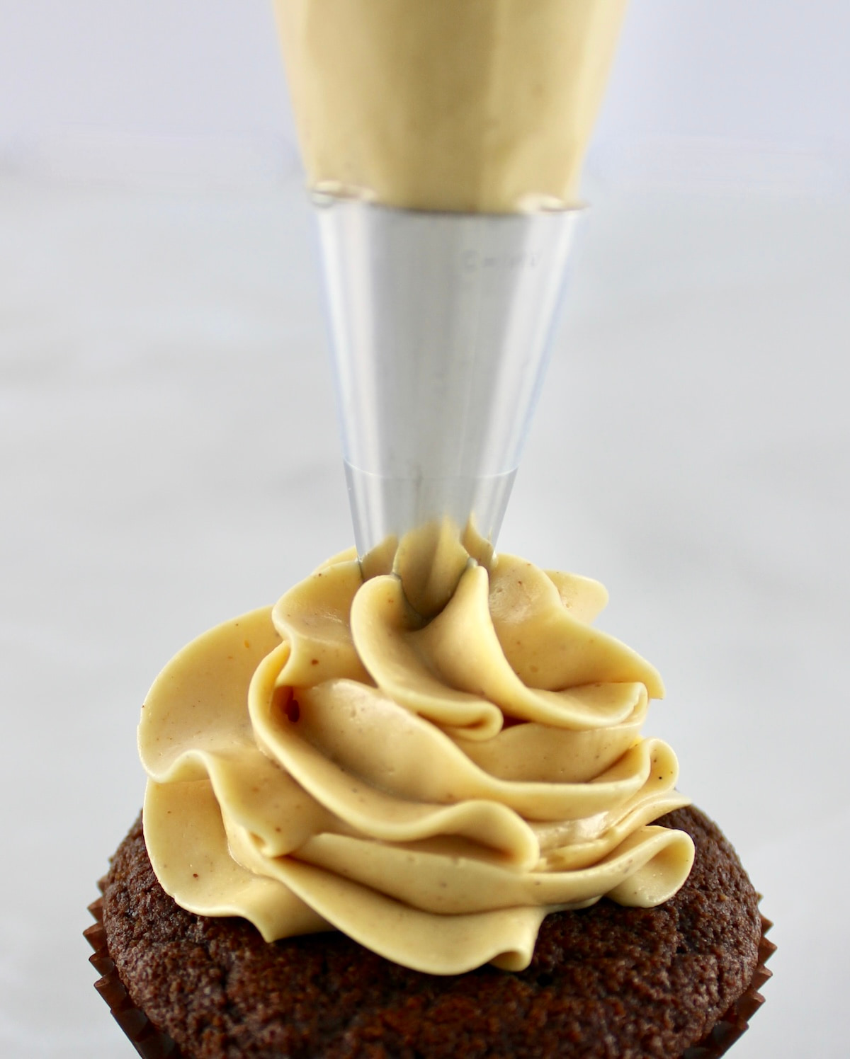 Keto Peanut Butter Frosting being piped onto chocolate cupcake