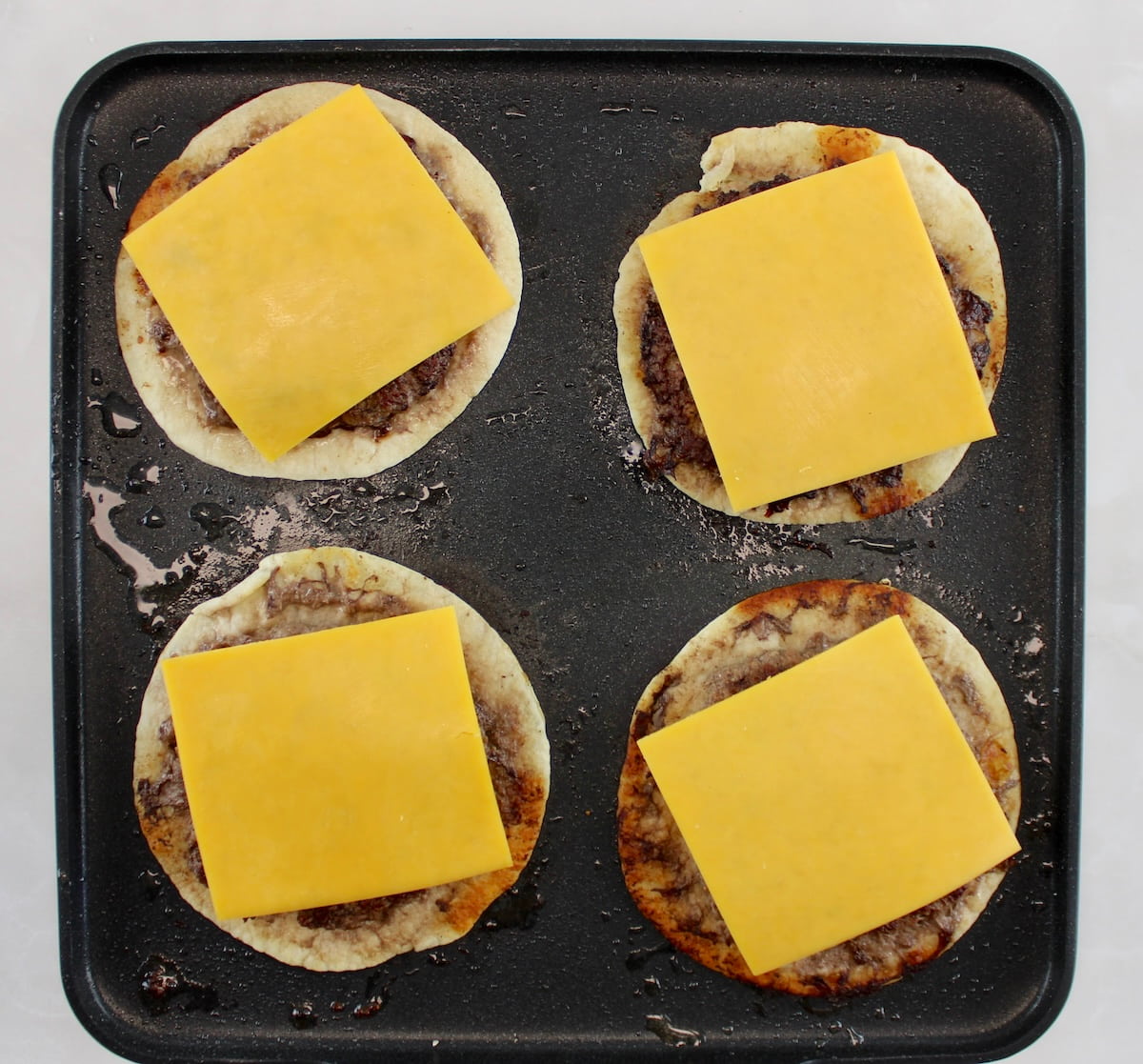 Keto Smash Burger Tacos with cheese on top cooking on griddle